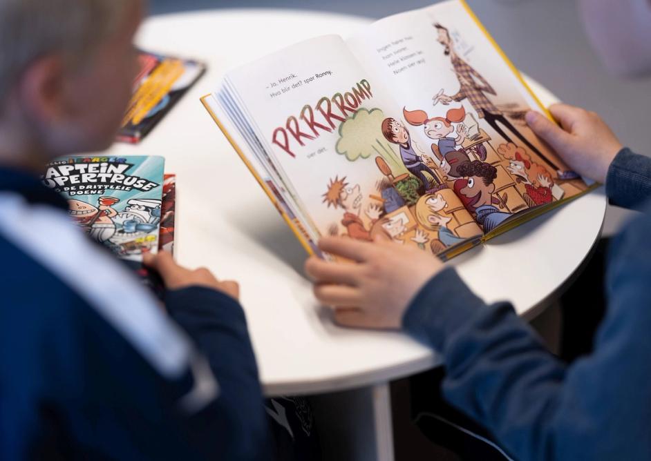 Foto av oppslått bok som leses av barn på biblioteket.