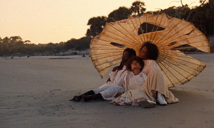 Utsnitt fra filmen Daughters of the Dust (1991) der 3 jenter sitter under en ødelagt parasoll