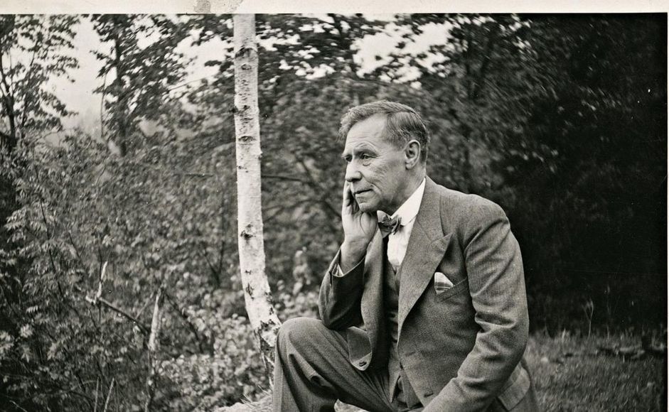 Olav Duun sittende på stein i skogen. Foto.