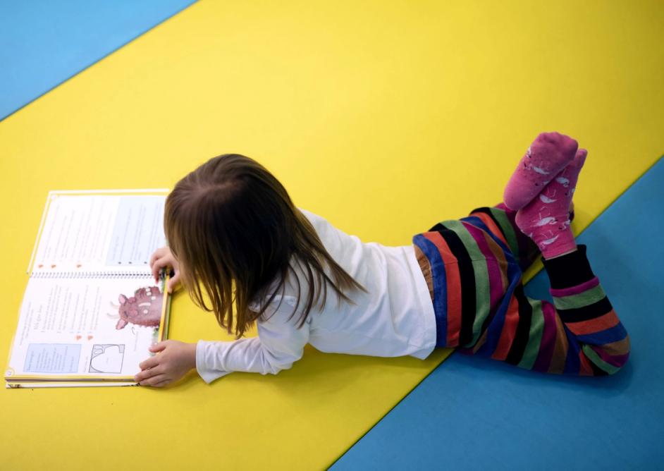 Jente ligger på gulvet i biblioteket og leser.